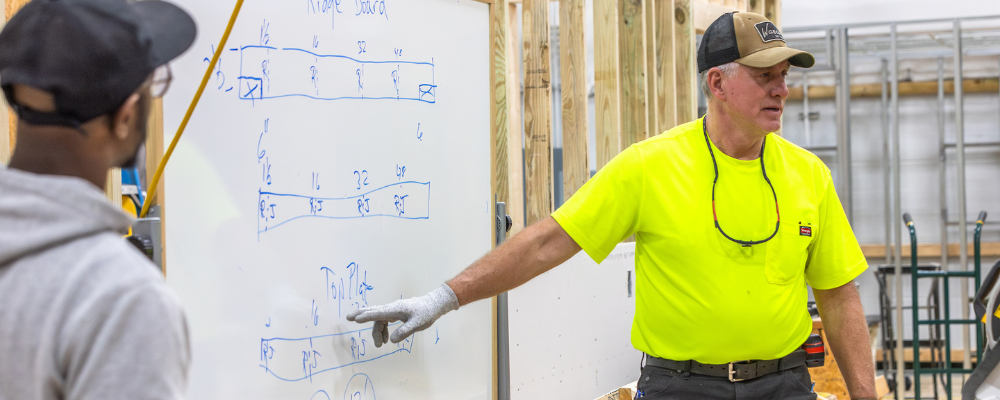 An instructor pointing at a white board containing information about basic construction math.